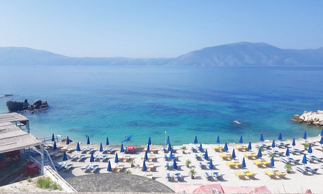 Rows of blue-and-yellow parasols and sunbeds on a beach club with a small rocky cove