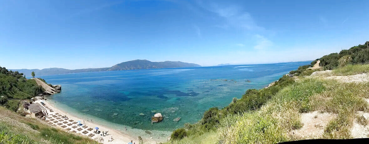Panoramic view of a turquoise cove with sunbeds on the beach and rocky headland on the right