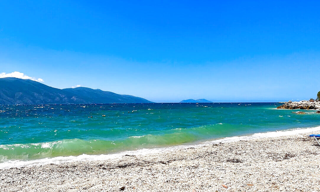 Small waves rolling onto a pebble beach under a bright sky