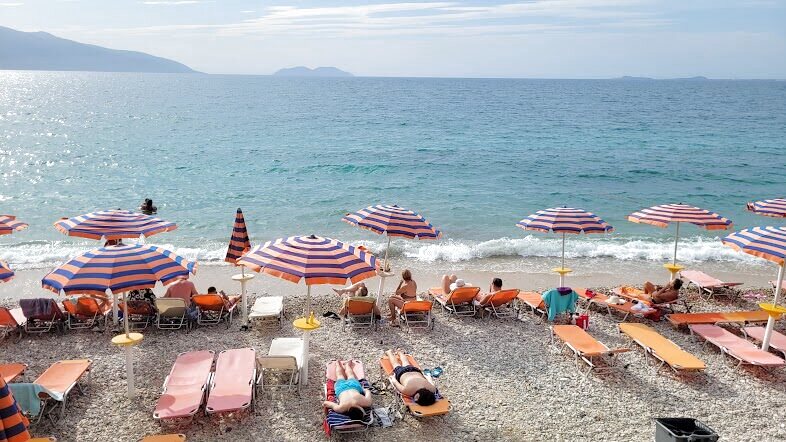 Striped parasols and sunbeds on a pebble beach with waves and an island on the horizon
