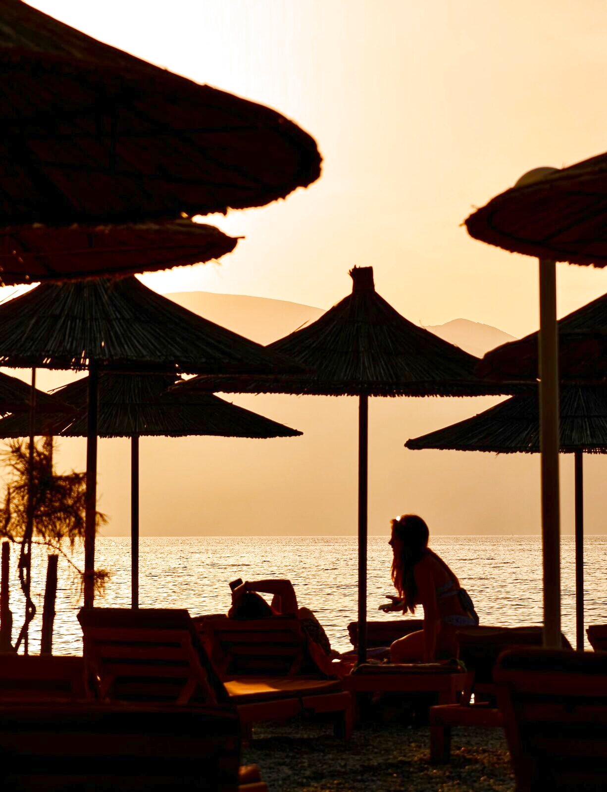 Reed parasols silhouetted against an orange sunset over the water
